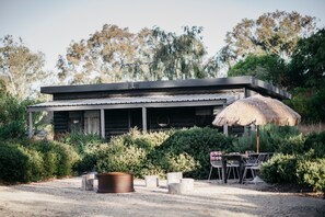 A rustic cabin with a thatched roof umbrella, surrounded by dense greenery.