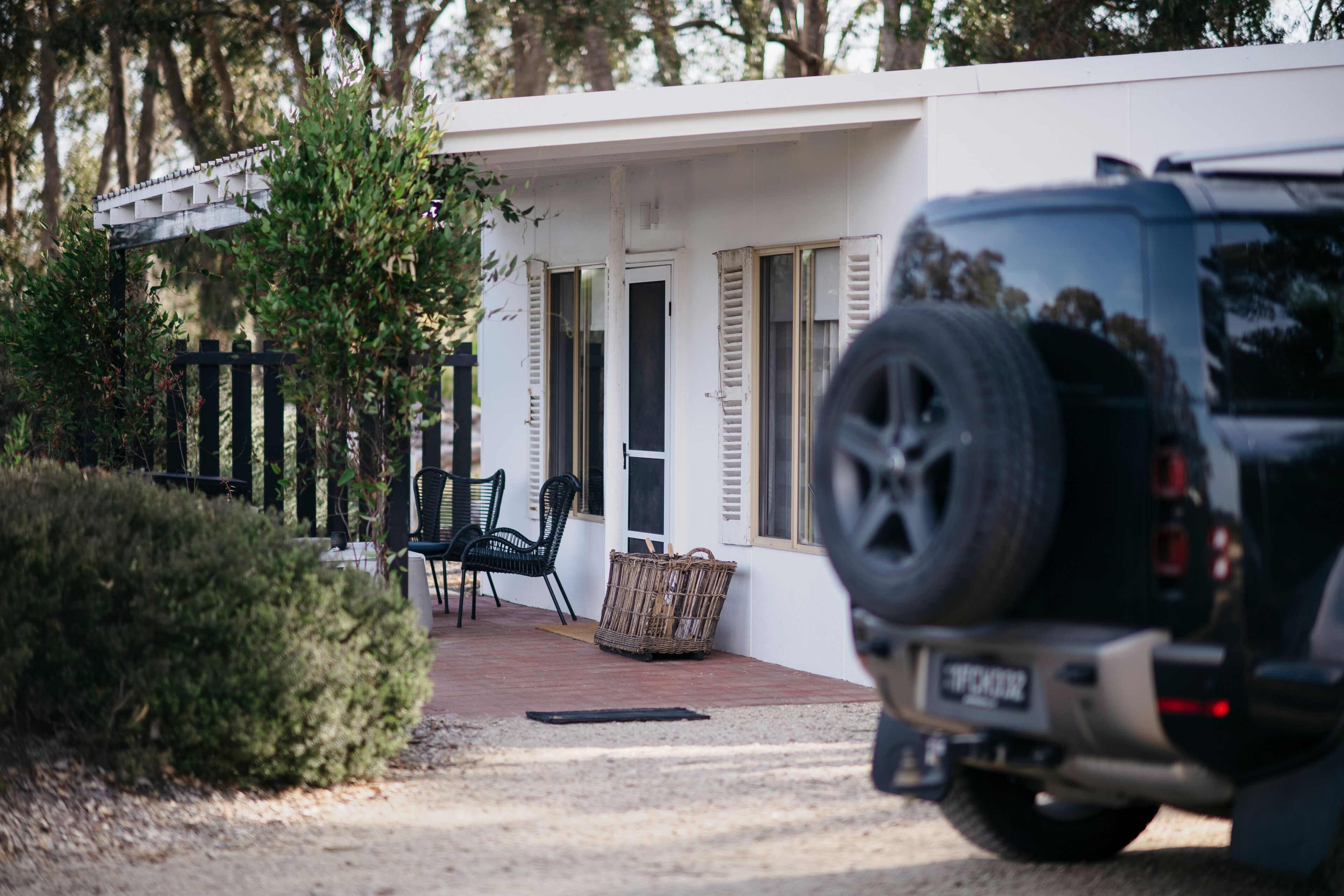A white building with a paved driveway, a black SUV parked in front, and a wicker basket near the entrance.