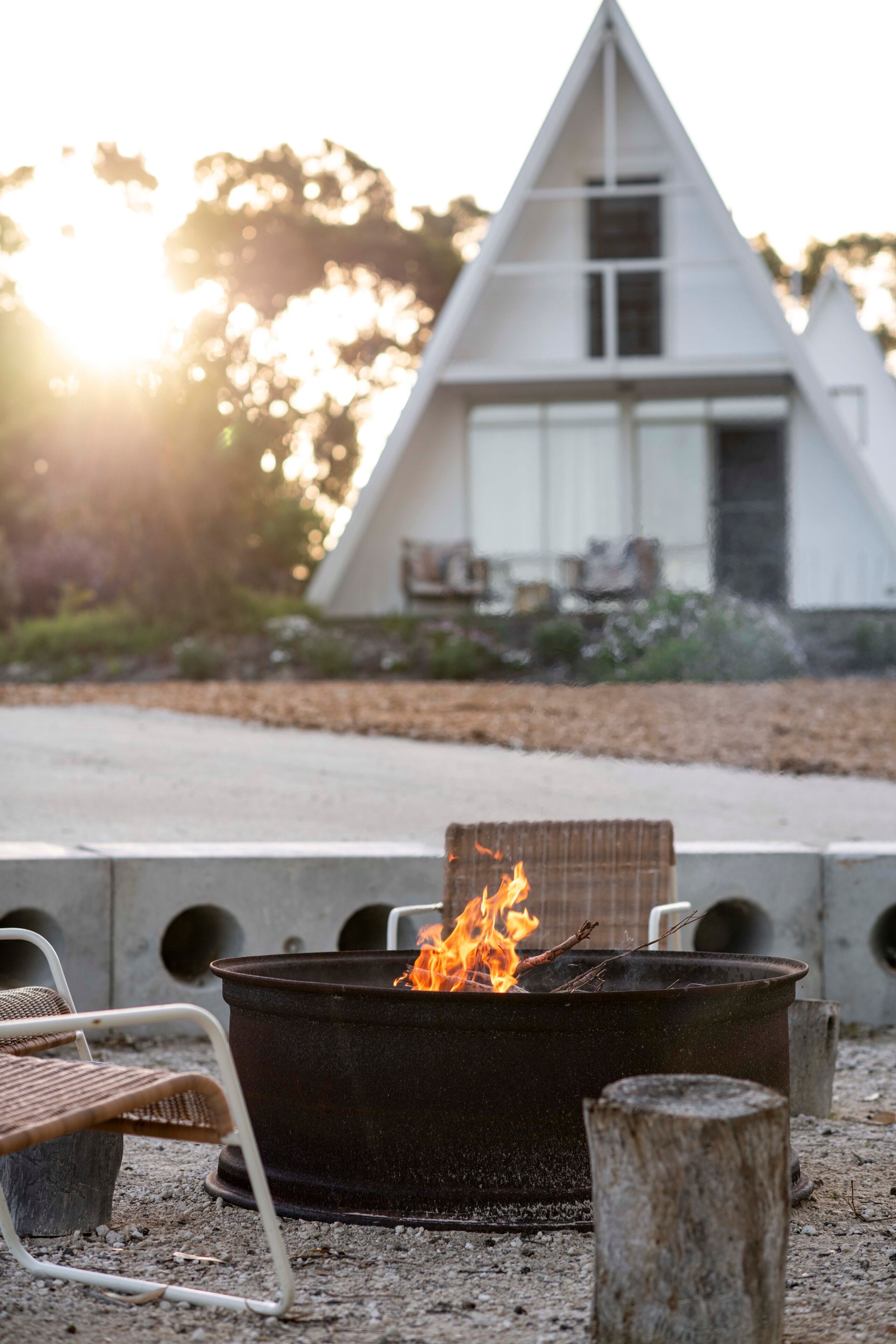A modern house with a triangular roof, a fire pit in the foreground, and outdoor furniture.