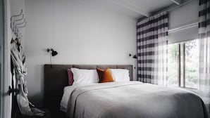 Een moderne slaapkamer met een groot bed, twee bedlampen, een raam met gordijnen en een kapstok met badjas.