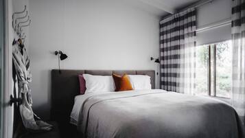 A modern bedroom with a large bed, two bedside lamps, a window with curtains, and a coat rack with a robe.