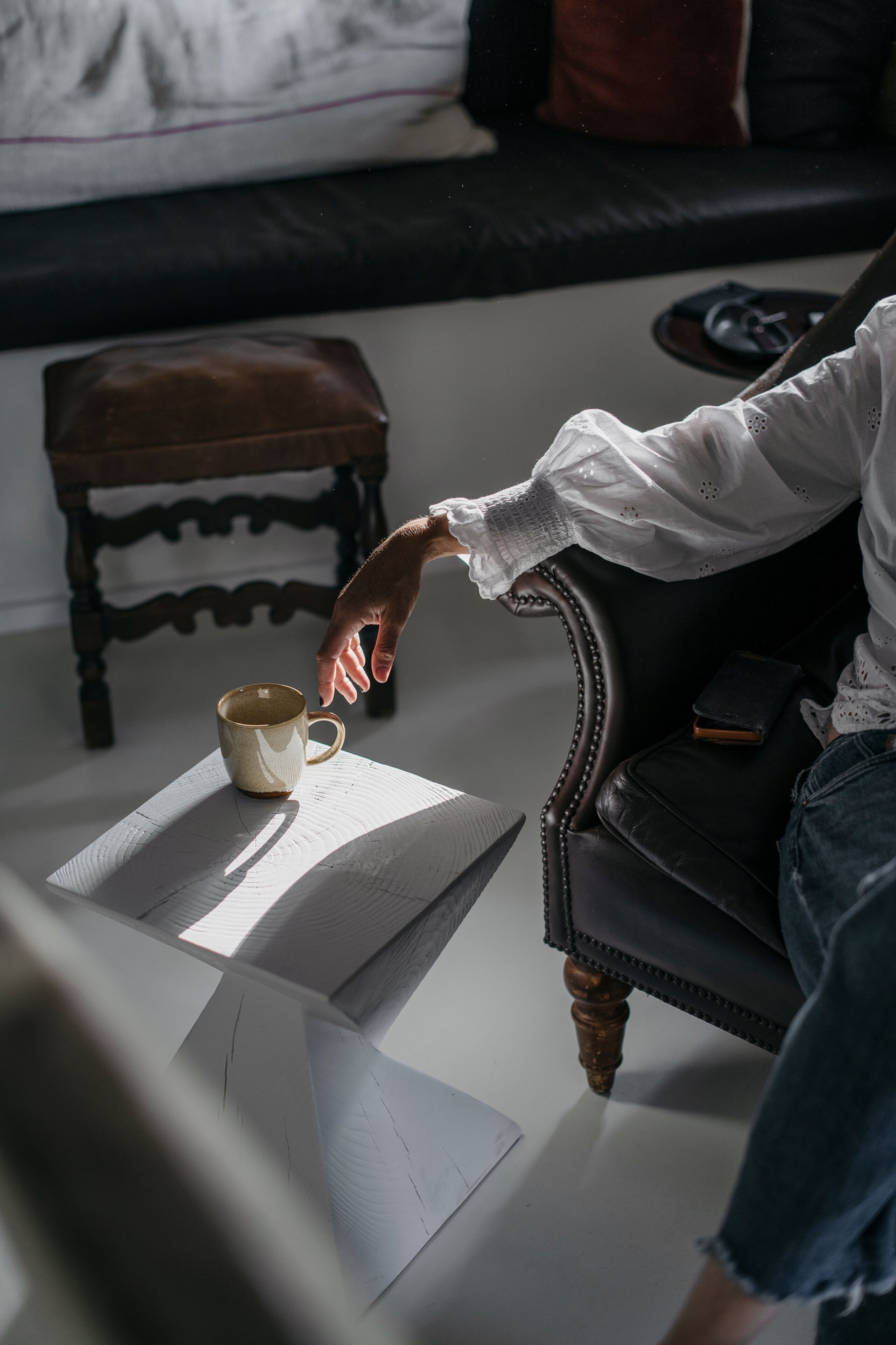 Una persona sentada en un sillón de cuero con una taza sobre una mesa frente a ella.