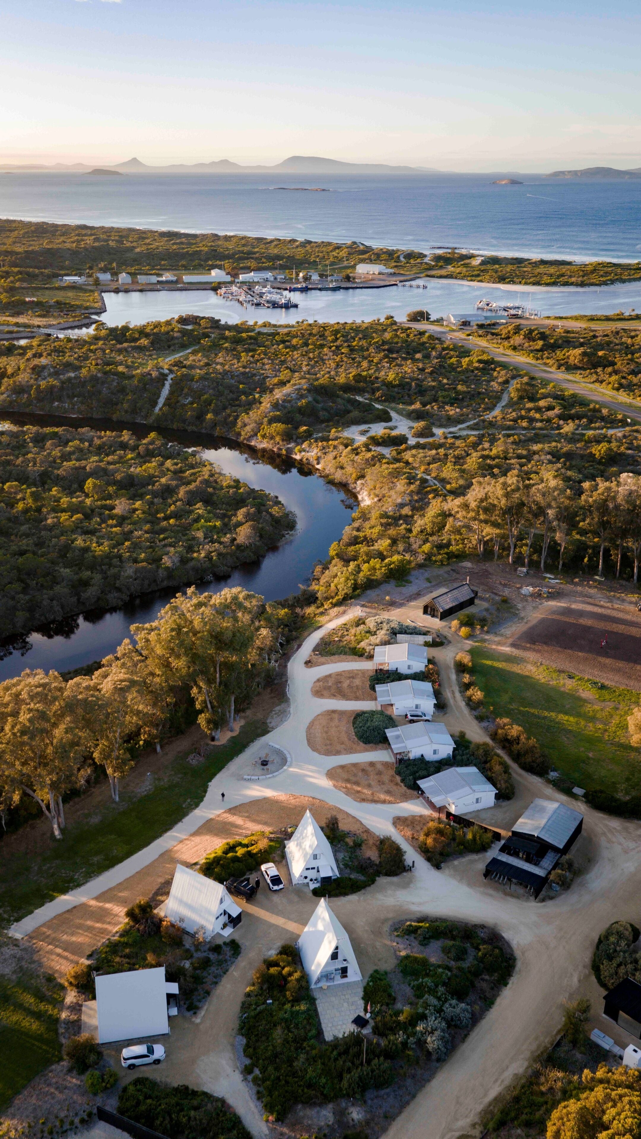 An aerial view of a coastal property with multiple white buildings, a marina, and a river.