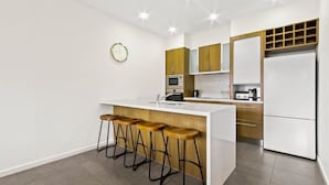A modern kitchen with a central island, bar stools, a microwave, a refrigerator, and wooden cabinets. - Blue Ice Chalet (Dinner Plain)