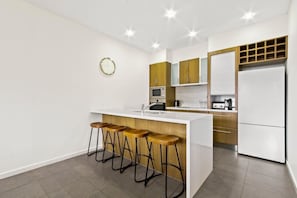Une cuisine moderne dotée d’un îlot central, de tabourets de bar, d’un four à micro-ondes, d’un réfrigérateur et d’armoires en bois.