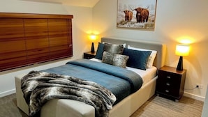 A bedroom with a bed, nightstands, a blanket, a painting, and a window with blinds. - Blue Ice Chalet (Dinner Plain)