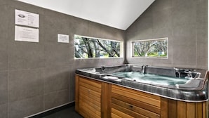 A spa room with a wooden tub, two windows with views of trees, and informational signs on the wall. - Blue Ice Chalet (Dinner Plain)