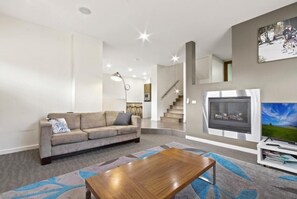 A modern living room with a sofa, a coffee table, a fireplace, a TV, and a staircase leading to another level. - Blue Ice Chalet (Dinner Plain)