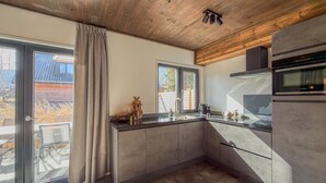 A modern kitchen with a large window, a built-in oven, and a wooden ceiling.