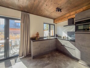 Eine moderne Küche mit großem Fenster, einem eingebauten Backofen und einer Holzbalkendecke.