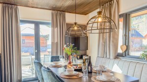 A dining area with a wooden table set for four, two pendant lights, and a view of the outdoors.