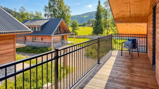 A wooden cabin with a balcony, a stone foundation, and a view of a green landscape.