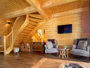 A wooden interior with a staircase, two armchairs, a coffee table, and a flat-screen TV mounted on the wall. - Chalet with garden located near Nassfeld area (Rattendorf)