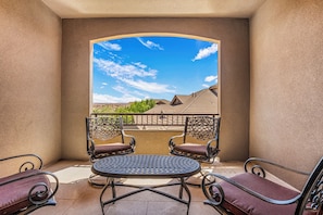 Ein Balkon mit rundem Tisch und zwei Stühlen, Blick auf eine hügelige Landschaft und einem wolkenlosen, blauen Himmel.