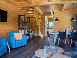 Ein gemütliches Holzinterieur mit einer Couch, einem Esstisch, Stühlen und einer Treppe.