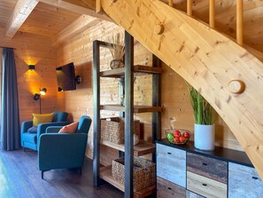 Ein Holzinnenraum mit einer Treppe, einem blauen Sofa, einem an der Wand montierten Fernseher und einer Fruchtschale.