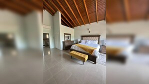 Un dormitorio con una cama grande, un cabecero de madera, un banco y un techo con vigas de madera.