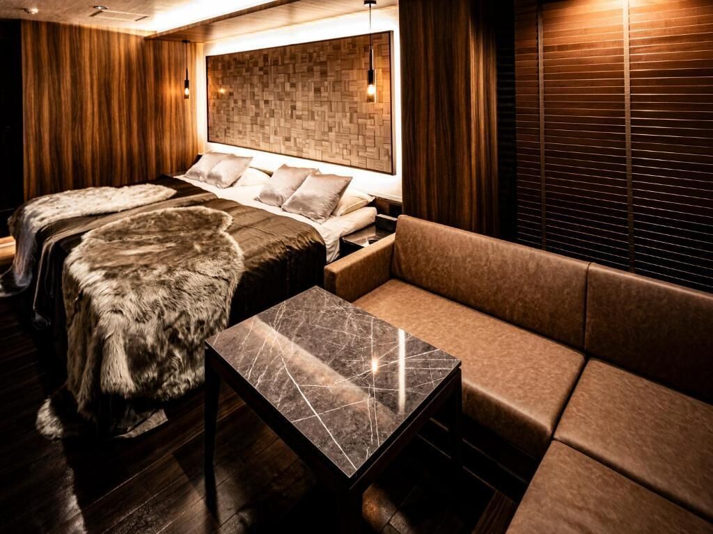 Quarto de hotel moderno com uma cama grande, um sofá, uma mesa de centro de mármore e um cobertor de pele.