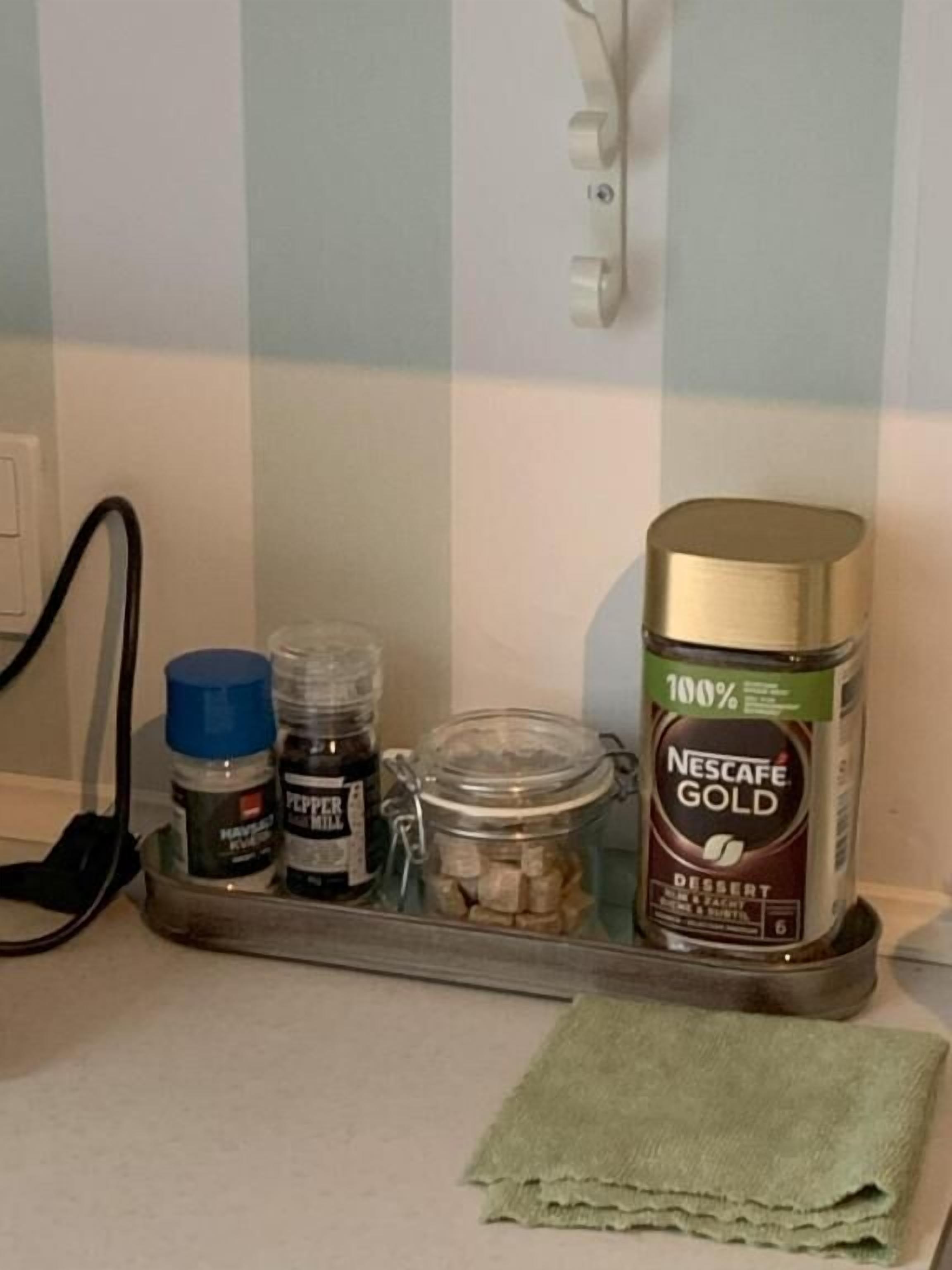 A kitchen counter with a Nescafe Gold can, a pepper mill, and a jar of sugar.