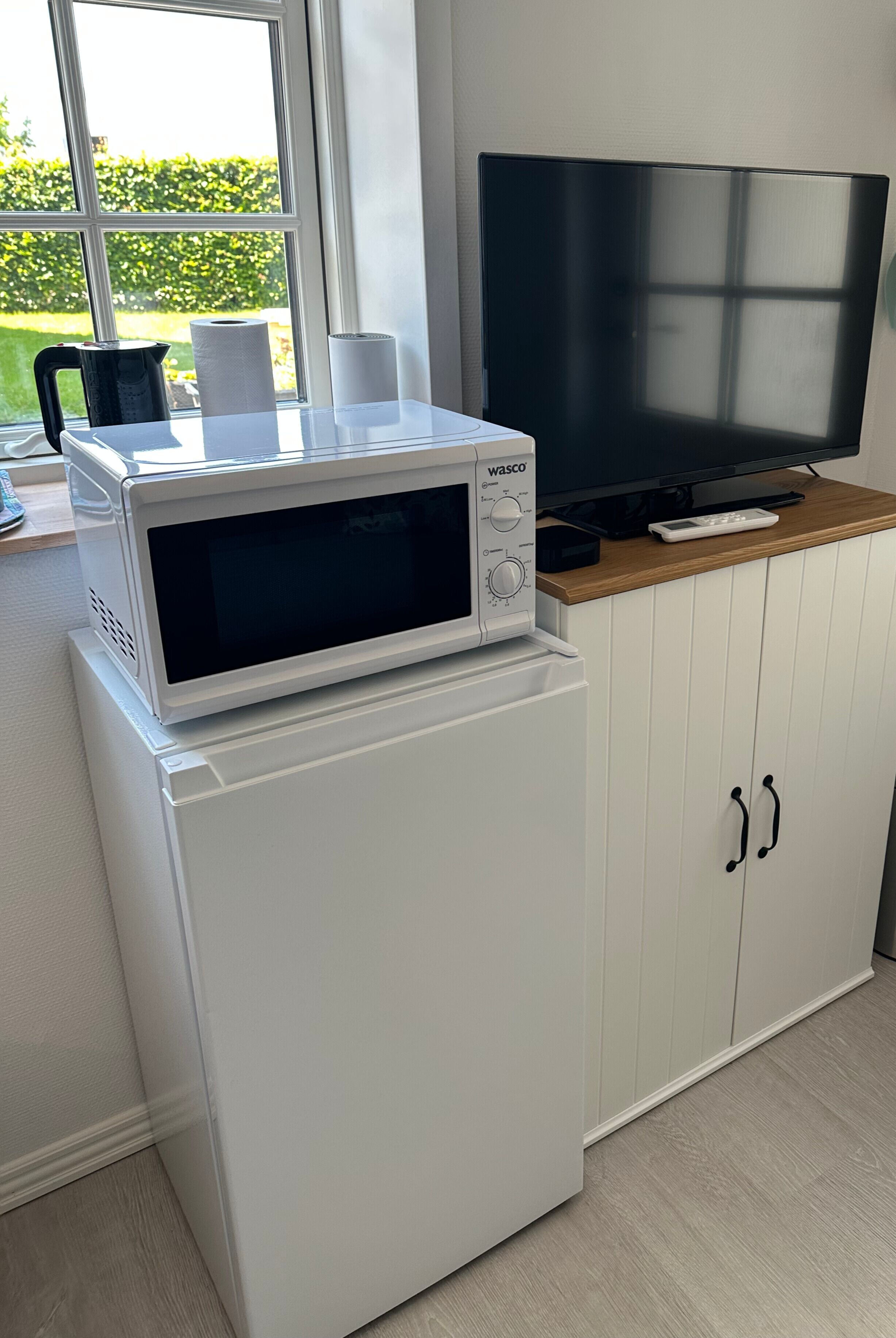 A compact kitchenette with a microwave, a small refrigerator, a TV, and a wooden countertop.