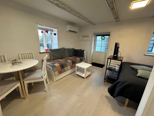 A compact living space with a sofa, a small table, and a TV stand. - Bed and Breakfast Den Gamle Lade I Hejls (Hejls)