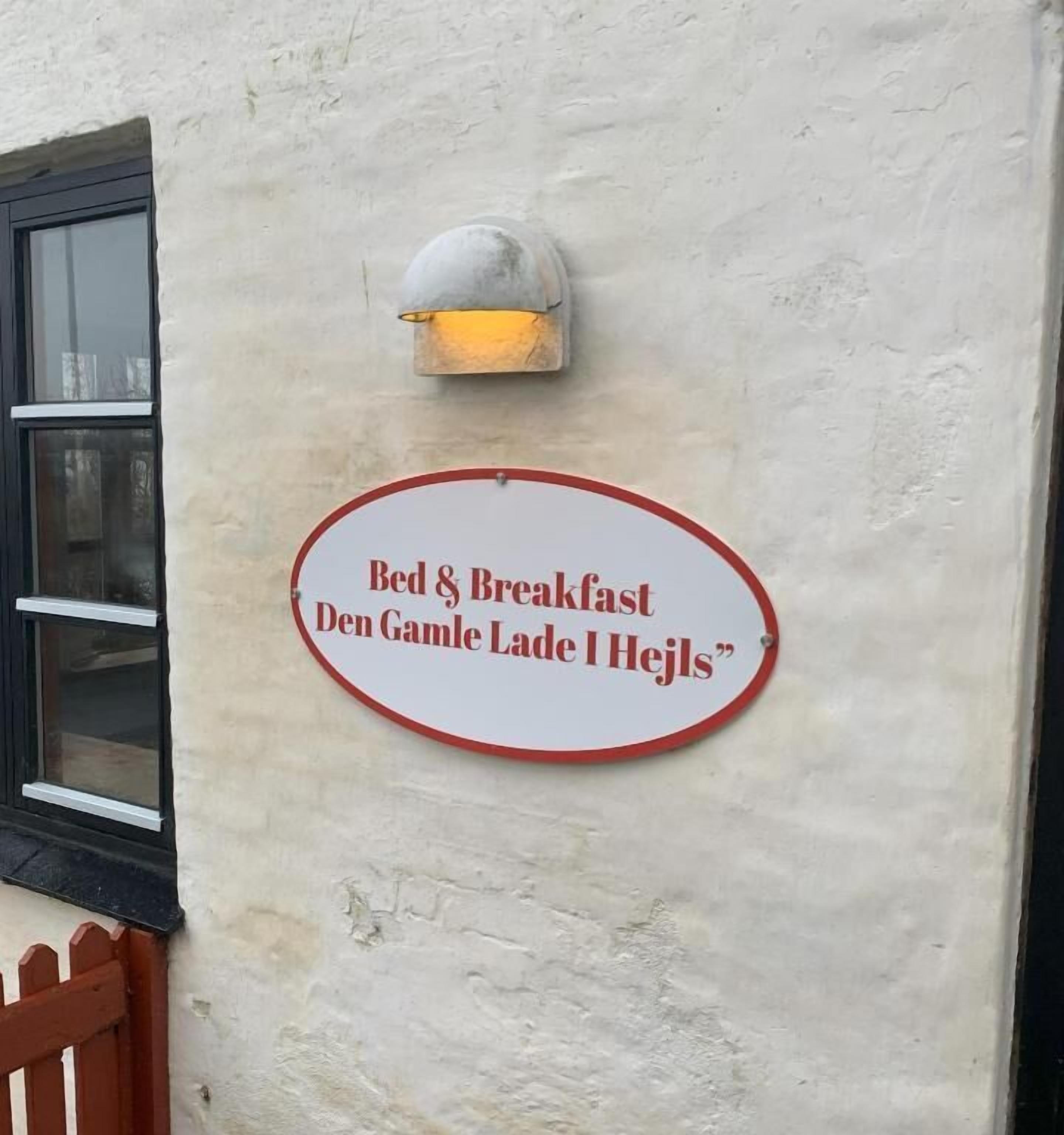 Skilt på en bygningsvæg, der reklamerer for 'Bed & Breakfast Den Gamle Lade I Hejls'.