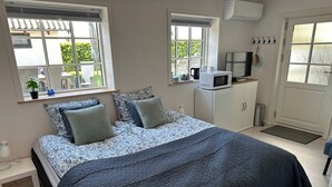 A bedroom with a bed, two windows, a microwave, a TV, and a small cabinet.