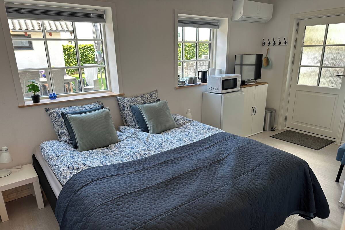 Ein Schlafzimmer mit einem Bett, zwei Fenstern, einer Mikrowelle, einem Fernseher und einem kleinen Schrank.