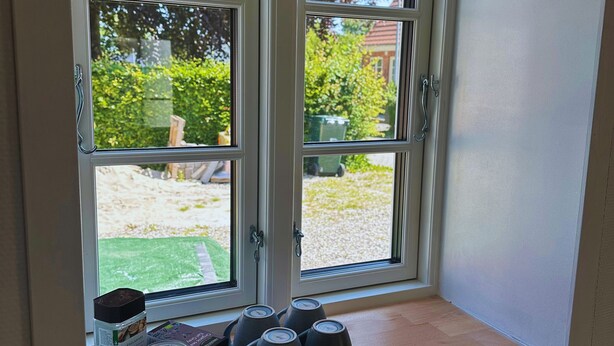 A room with a large window, a small seating area with cushions, and a coffee maker on the windowsill.