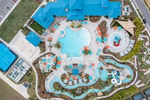Ein Luftbild eines Resorts mit einem zentral gelegenen Schwimmbad, einer Wasserrutsche und einem Tennisplatz.