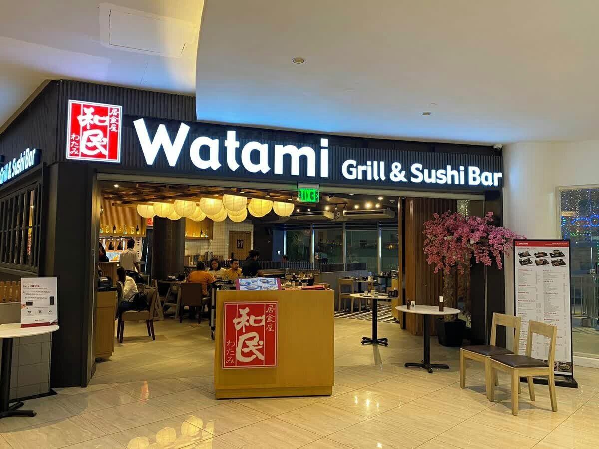 A restaurant named 'Watami Grill & Sushi Bar' with a signboard, a reception desk, and a seating area with tables and chairs.