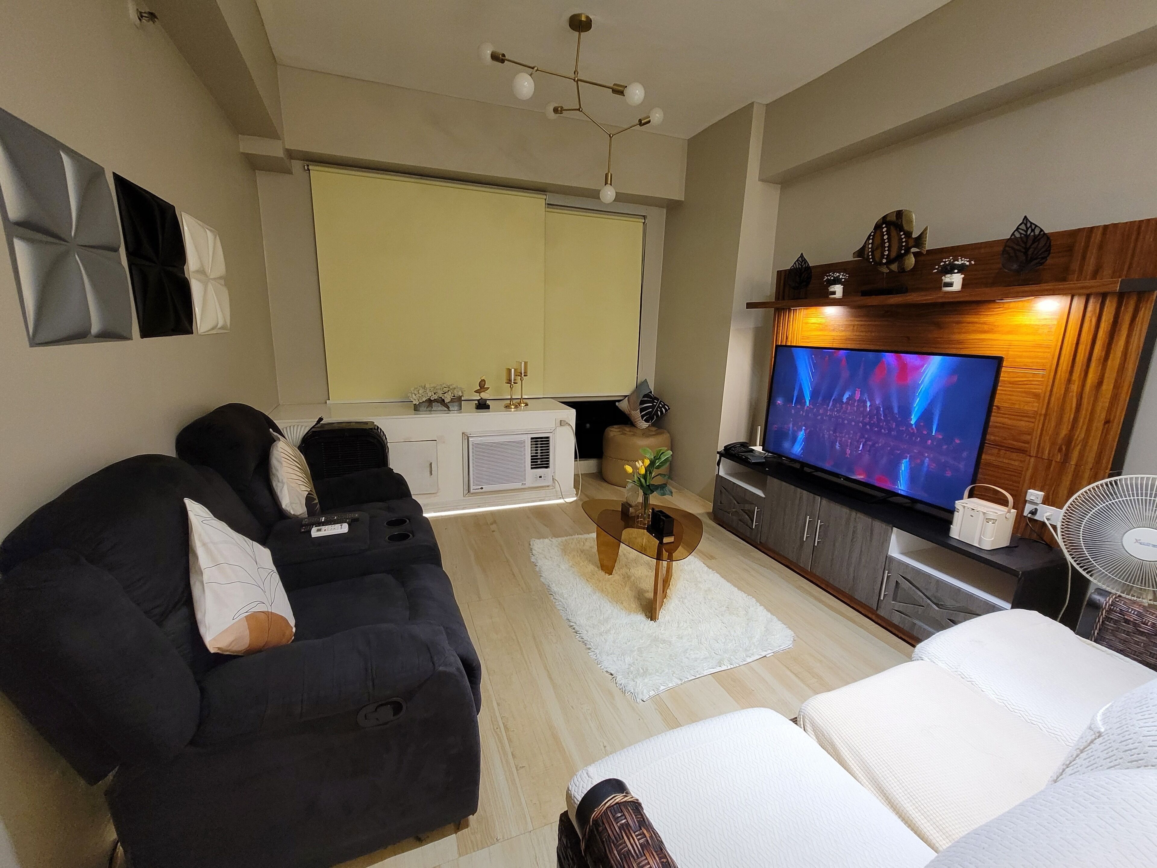 A living room with a black sofa, a white sofa, a TV, and a wooden entertainment unit.