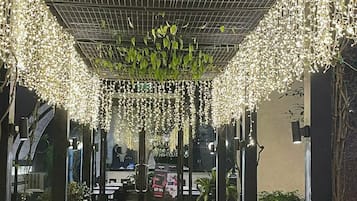 An indoor pathway with a ceiling covered in hanging lights and greenery, leading to a reception area.