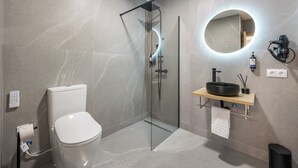 Un baño moderno con ducha de vidrio, inodoro y tocador con un espejo redondo.