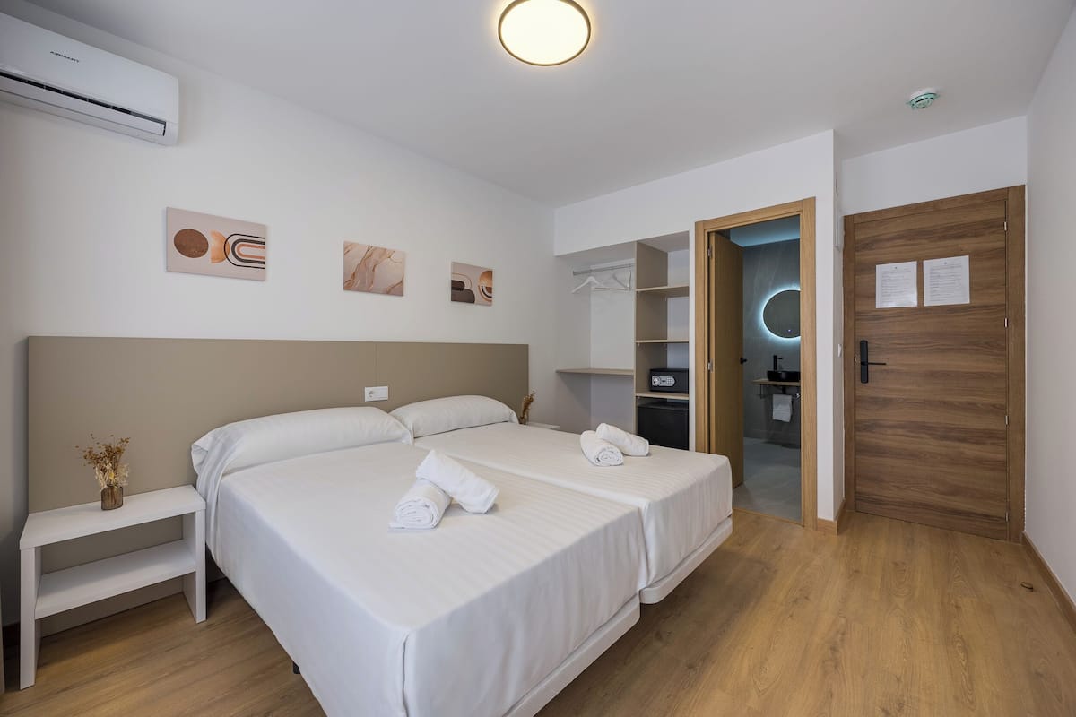 A modern hotel room with a large bed, bedside tables, a wardrobe, and a bathroom visible through an open door.