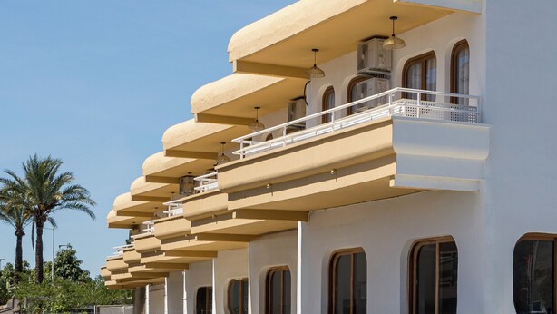 Un edificio de varios pisos con balcones, ventanas arqueadas y techo plano.
