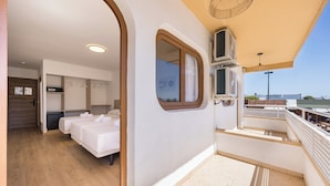 Un balcón con vistas, una habitación con dos camas y un ventanal pequeño.
