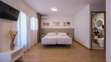 Une chambre d’hôtel avec un grand lit, une télévision, une table de chevet, un miroir et une salle de bain visible à travers une porte ouverte.