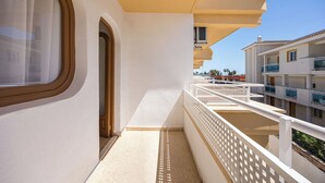 Un balcón con barandilla blanca, una ventana con marco marrón y vistas despejadas a edificios cercanos.