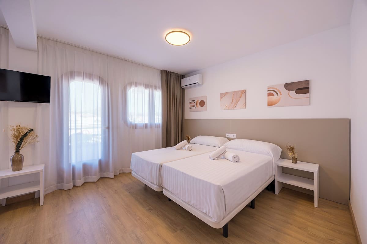 A double bed with white linens, a flat-screen TV mounted on the wall, and a ceiling light fixture.