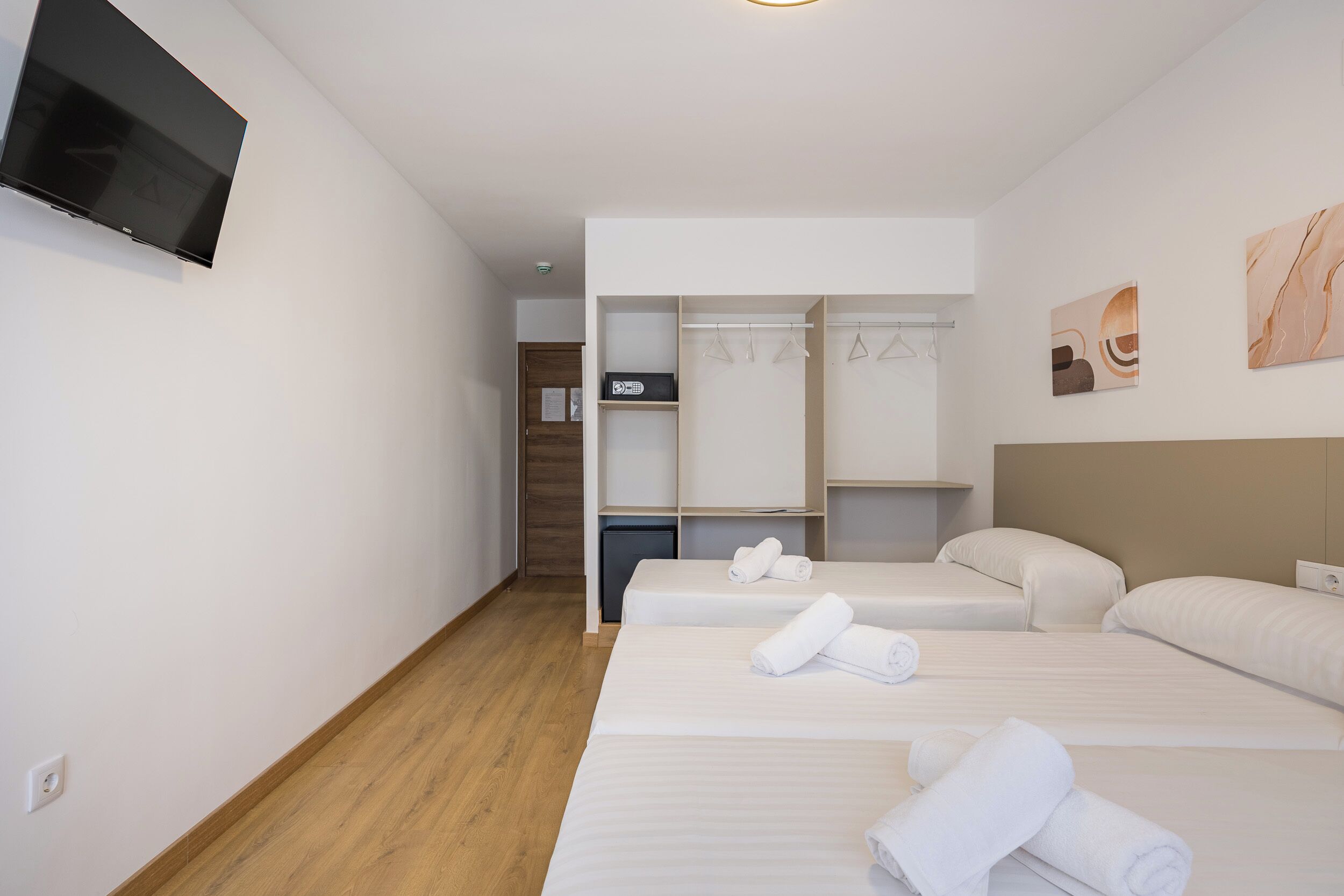 A hotel room with a TV, two beds with towels, a closet, and artwork on the wall.