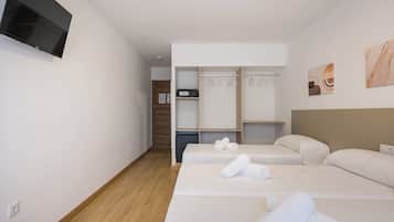 A hotel room with a TV, two beds with towels, a closet, and artwork on the wall.