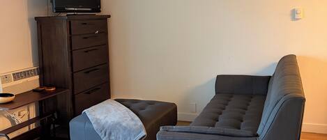 A living room with a flat-screen TV, a dark wooden cabinet, a gray sofa, a small wooden table, and a ceiling fan.