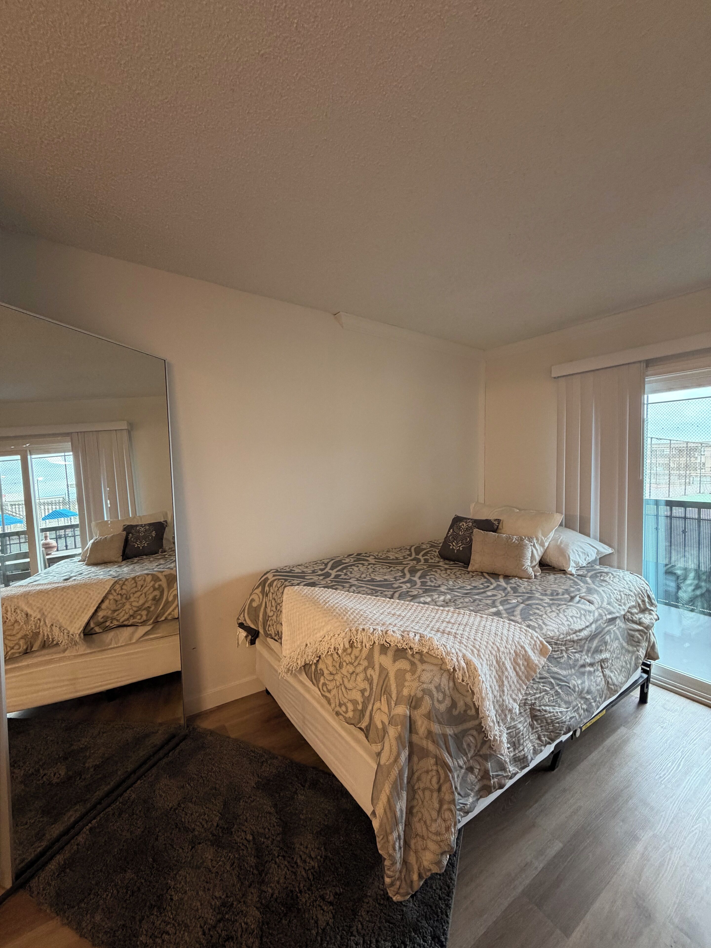 Een slaapkamer met een groot bed, een spiegel, een raam met gordijnen en uitzicht op buiten.