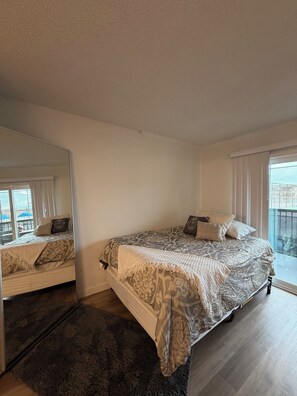 Ein Schlafzimmer mit einem großen Bett, einem Spiegel, einem Fenster mit Vorhängen und Blick nach draußen.