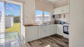 A kitchen with white cabinets, a microwave, a stove, and a window with blinds. - Melinga in Sussex Inlet (Sussex Inlet)