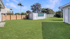 A backyard with a well-maintained lawn, a brick wall, and a white shed. - Melinga in Sussex Inlet (Sussex Inlet)