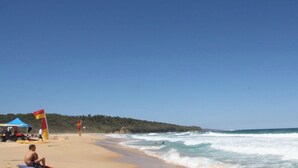 Una spiaggia con cielo sereno, una riva sabbiosa e onde che si infrangono sulla battigia.