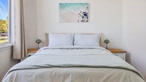 Un letto rifatto con cura, un cuscino a righe, una lampada da comodino e un quadro appeso al muro.