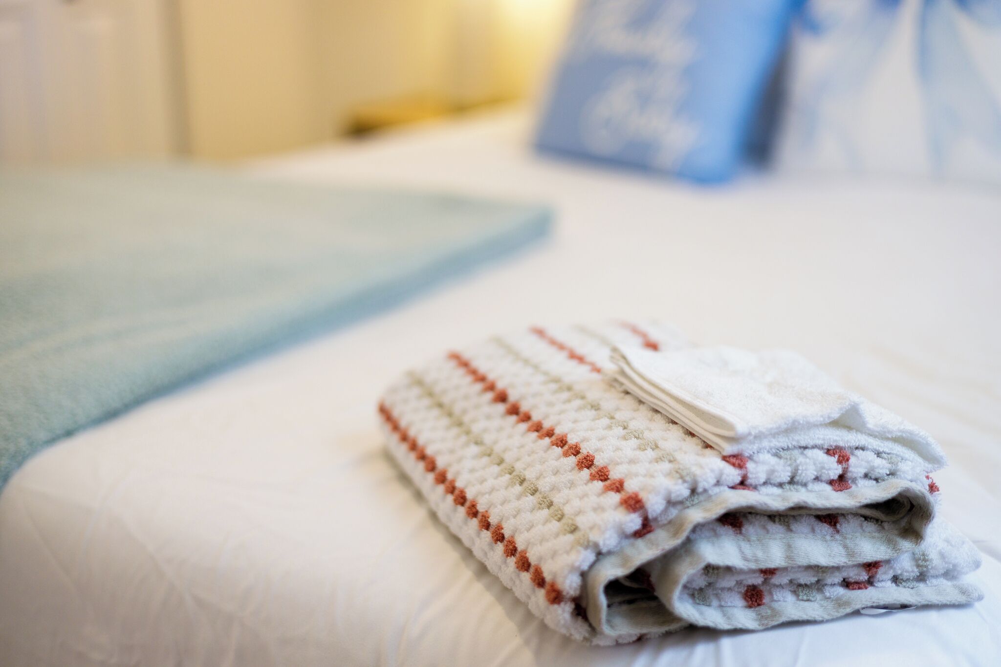 Ein ordentlich gefaltetes Handtuch auf einem Bett mit einer hellblauen Decke.